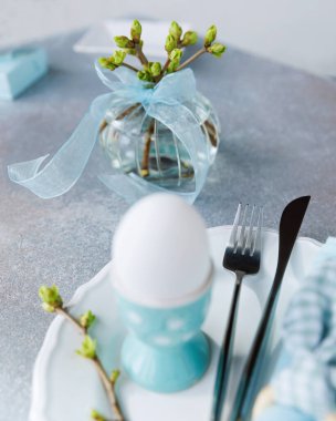 Mavi tutacaklı paskalya yumurtasına yakın çekim. Yay vazosu ve tabağında çatal bıçak var.