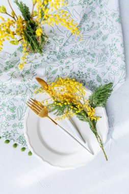 Altın çatal bıçak takımı, mimoza çiçekleri ve çiçek peçetesi olan parlak ve narin bir bahar sofrası. Paskalya ve Anneler Günü için mükemmel..