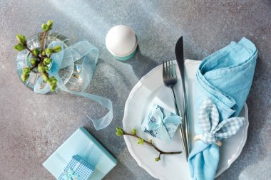 Yumurtalı Paskalya kahvaltısı masası, mavi hediye kutuları, peçete, tabak, tomurcuk ve kurdele vazosu.