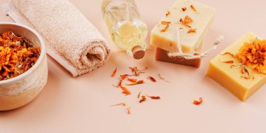 Doğal sabun barları, takvim yaprakları, bitkisel yağ, rulo havlu ve yumuşak pastel arka planda kadife çiçeği.