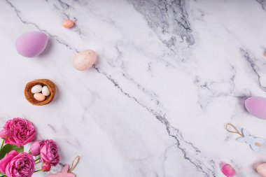 Süslü Paskalya yumurtaları, pembe güller, tavşan süsleri ve şeker yumurtalı mini yuvaların üst görüntüsü.