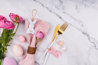 Düz Paskalya masa elementleri arasında çatal bıçak takımı, tavşan peçete halkası, benekli yumurta ve pembe çiçekler var.