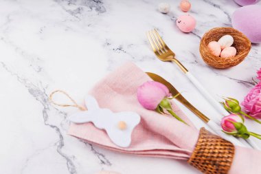 Pastel Paskalya yumurtaları, tavşancık süsleri, pembe çiçekler ve mermer üzerinde şenlik sofra takımı.