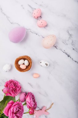 Pembe ve mor Paskalya yumurtaları, benekli şeker yumurtaları, güller ve dokunmuş tavşan süslemeleri.