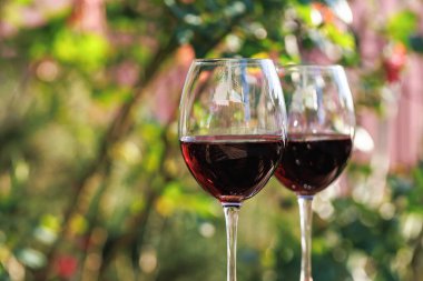 Renkli, bulanık arka planı ve yumuşak doğal ışığı olan keskin odaklı iki kadeh kırmızı şarap.