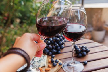 İki kırmızı şarap kadehi ahşap masada üzümlü, mavi peynirli ve bademli tost.