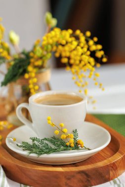 Basit ama zarif bir kahve sahnesi, bir fincan espresso, bir ahşap tepsi, ve bir buket mimoza çiçeği, samimi ve şenlikli bir bahar atmosferi yakalıyor..