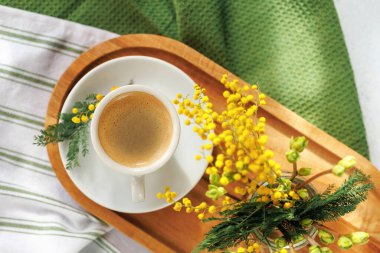 Taze mimoza çiçekleri ve yumuşak tekstil ile süslenmiş, ahşap tepside bir fincan espresso ile sıcacık bir bahar sabahı..