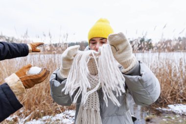 Kışlık montlu neşeli bir kadın. Yüzünde püsküllü bir eşarp var.