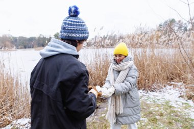 Genç bir çocuk ve orta yaşlı bir kadın kışın doğal ortamında neşeli bir bağ kurarken gülümsüyor ve kartopu paylaşıyor.