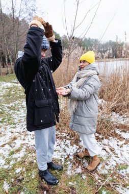 Anne gülümserken, genç çocuk soğuk havada hava aktivitesi sırasında ellerine kar düşürür.