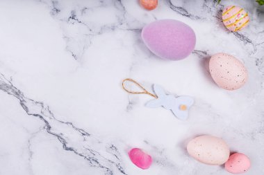 Beyaz mermer yüzeyde pastel yumurtalar, tavşan süsü ve çiçek yapraklarıyla minimum Paskalya kompozisyonu