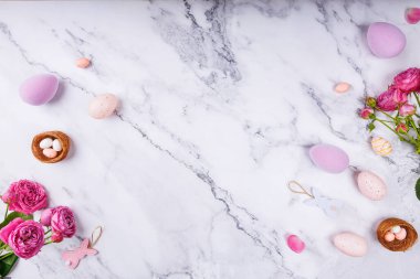 Pastel renkli Paskalya yumurtaları, pembe güller, yuvalarda şeker yumurtaları, ve beyaz mermer üzerinde tavşan süslemeleri