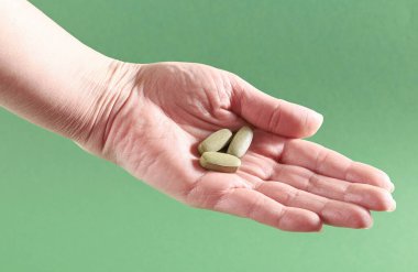 Yeşil arka planda bitkisel takviye tabletleri tutan kadın el, doğal vitaminleri, biyohack sağlık hizmetleri konseptini, fotokopi alanı ile kapatır.
