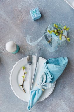 Tabak, yumurta, kurdele vazosu, çatal bıçak takımı ve pastel renkli hediye kutusu olan dikey yay masa örtüsü.