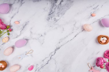 Dağınık pastel Paskalya yumurtaları, yuvalarda şeker yumurtaları, tavşan süsleri ve temiz mermer yüzeyde pembe güller.