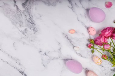 Yumuşak pastel Paskalya yumurtaları, yuvada şeker yumurtaları ve mermer arka planda canlı pembe çiçekler.