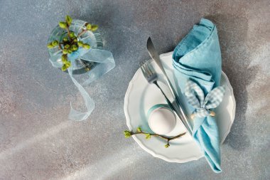 Yumurta, çatal bıçak, mavi peçete ve tomurcuklanan dallı bahar tatili masasının genel manzarası.