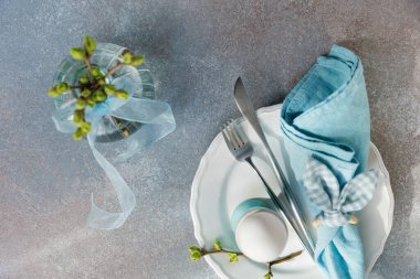 Beyaz yumurta, mavi peçete, çatal bıçak takımı ve yeni tomurcuklanan vazo ile bahar Paskalya masası.