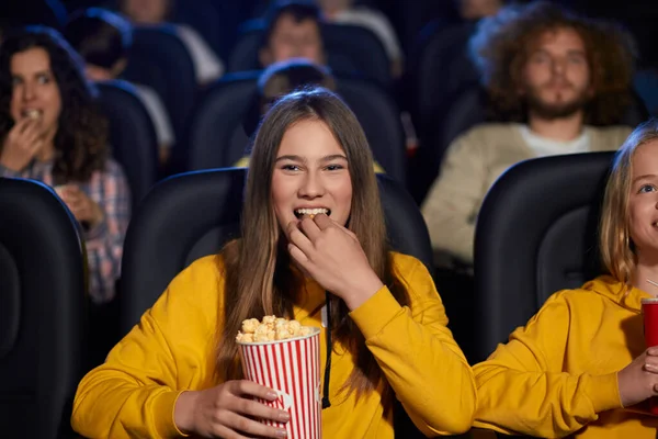 Young laughing girl eating popcorn in movie theater.