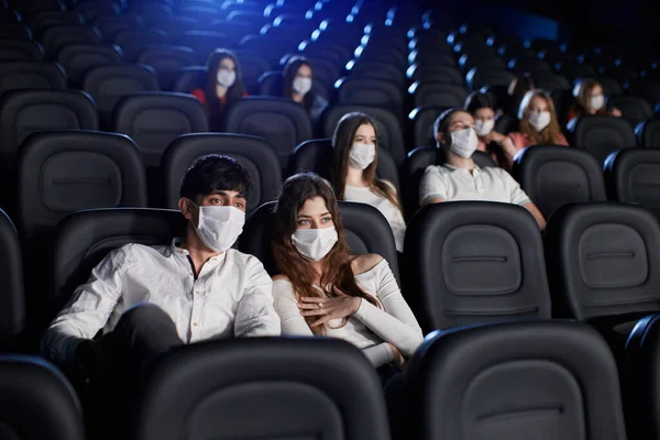 Audience wearing face masks enjoying time in cinema.
