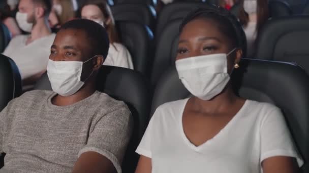 Afrikai pár visel arc maszkok élvezi komédia a moziban. — Stock videók