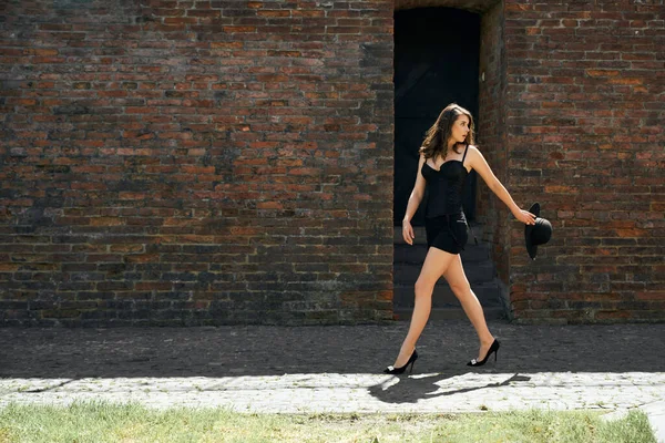 Mujer vistiendo vestido caminando cerca de pared de ladrillo viejo. —  Fotos de Stock