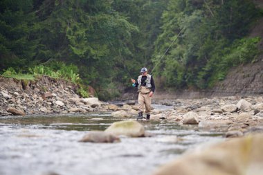 İki profesyonel çubukla nehirde yürüyen bir balıkçı.
