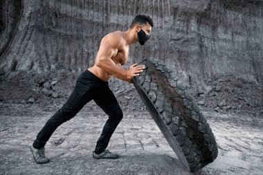 Siyah maskeli atletik adam dışarıda lastik taşıyor.