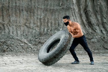 Çıplak gövdeli güçlü bir adam ağır lastikleri dışarı itiyor.