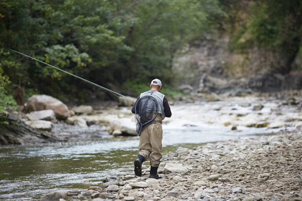 Vista trasera del pescador caminando a lo largo del río de montaña con caña — Foto de Stock