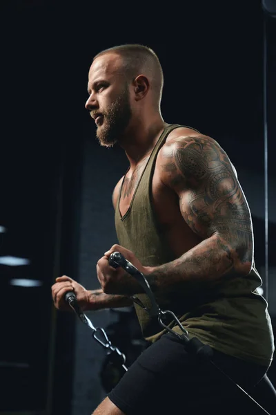 Tatuoitu kehonrakentaja tekee alhainen kaapeli crossover liikunta. — kuvapankkivalokuva