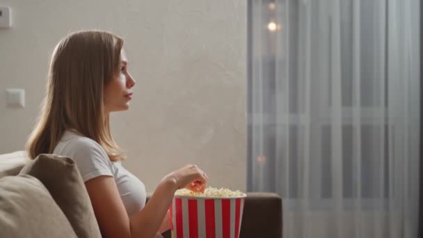 Žena sedí na gauči s popcornem a dívá se na film — Stock video