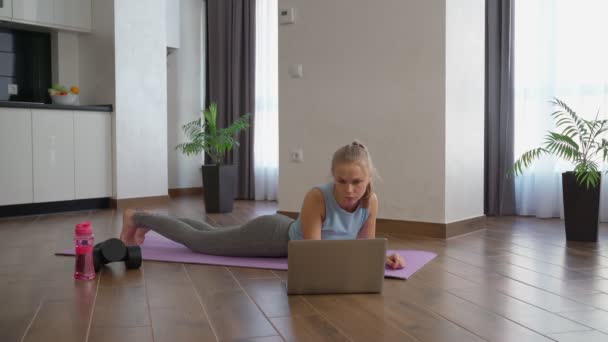 Wanita melakukan yoga papan dan menonton tutorial pada laptop — Stok Video