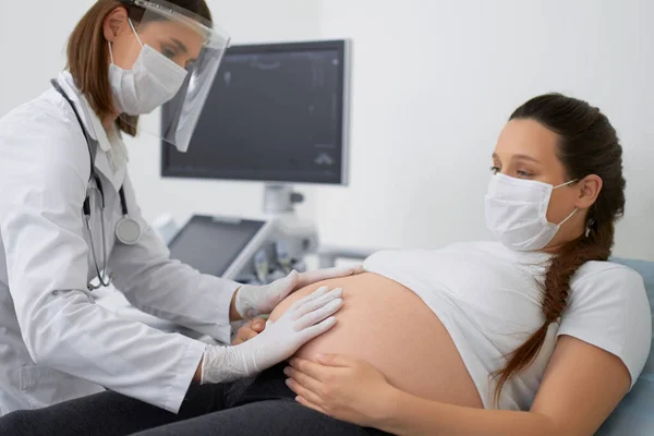 Гинеколог в маске делает пальпацию беременной женщины — стоковое фото