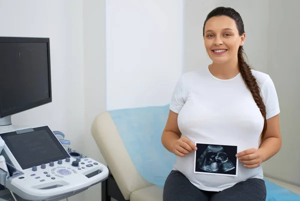 Adorable lady in expectation holding ultrasound photo