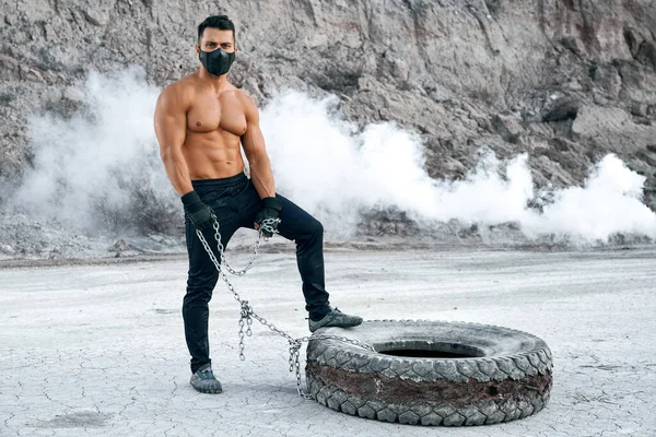 Hombre musculoso con mascarilla posando cerca de neumático grande — Foto de Stock