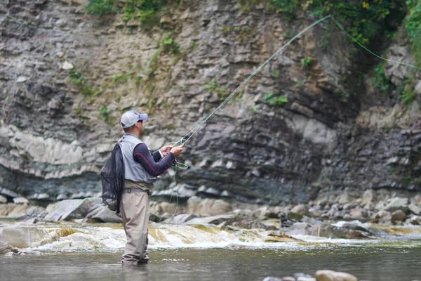 Hombre maduro pesca con mosca en el río de montaña durante el día de verano — Foto de Stock