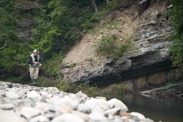 Man met behulp van staaf vliegen vissen in ruwe rivier tussen de bergen — Stockfoto
