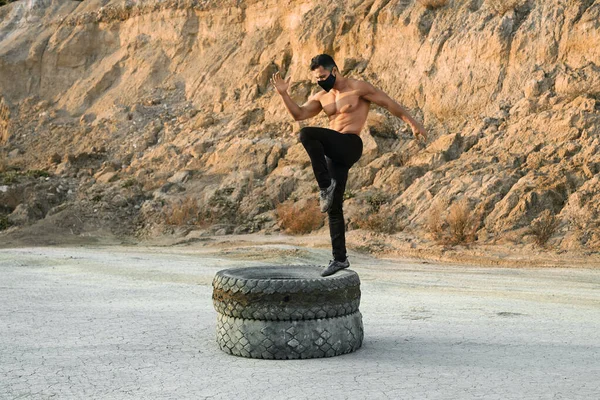 Hombre atlético con máscara facial piernas de entrenamiento en neumáticos — Foto de Stock