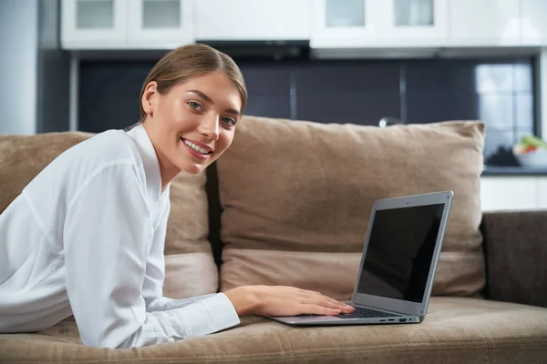 Mulher bonita deitada no sofá com laptop sem fio — Fotografia de Stock