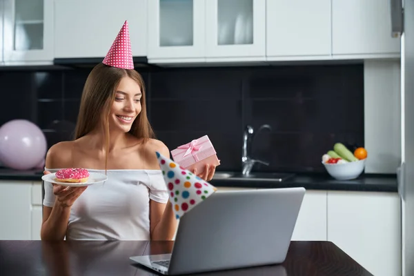 Mujer sosteniendo donut y caja de regalo durante la fiesta en línea —  Fotos de Stock