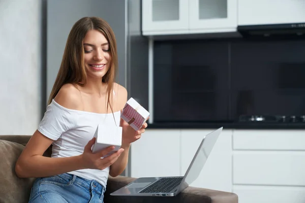 Senhora sentada no sofá com laptop e desembalagem presente de aniversário — Fotografia de Stock