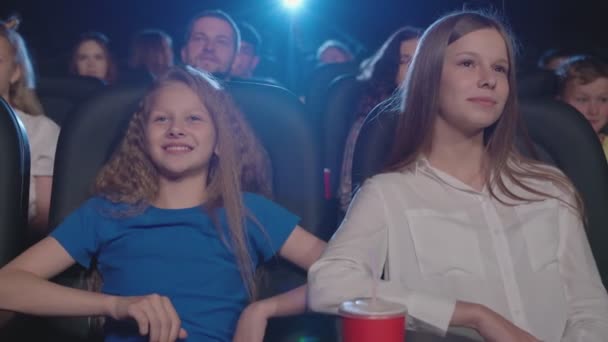 Mladá smějící se dívka s mladší sestrou v kině. — Stock video