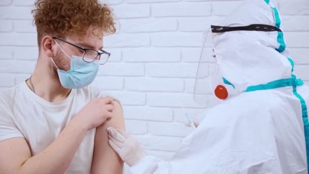 젊은 남자를 위한 covid-19 에서 주사를 만드는 보호용 양복과 마스크를 하는 의사. — 비디오