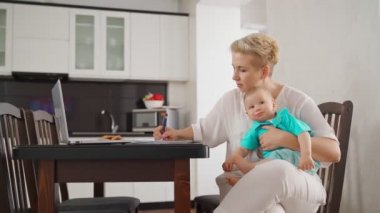 Bilgisayarda görüntülü sohbet sırasında bebeği taşıyan meşgul bir kadın.