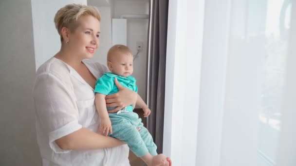 Charmig kvinna håller baby och tittar på fönstret — Stockvideo