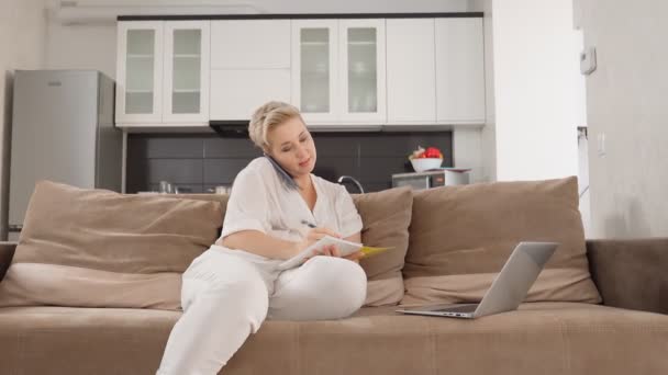 Vrouw praten op mobiel en werken op laptop van thuis — Stockvideo
