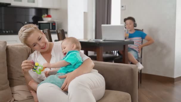 Mère divertissant plus jeune fils tandis que l'aîné en utilisant un ordinateur portable — Video