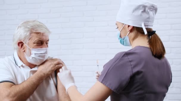 Kvinnlig sjuksköterska i uniform som ger vaccin för patient i skyddsmask. — Stockvideo